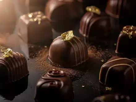 Nahaufnahme von luxuriösen Schokoladenpralinen, einige mit Goldfolie, auf einer dunklen, reflektierenden Oberfläche. - Foto: über boerse-global.de