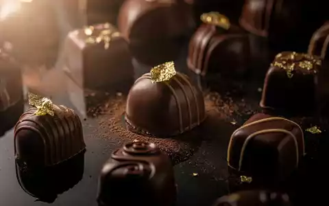 Nahaufnahme von luxuriösen Schokoladenpralinen, einige mit Goldfolie, auf einer dunklen, reflektierenden Oberfläche. - Foto: über boerse-global.de