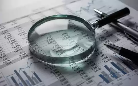 Eine Nahaufnahme einer Lupe über einem Finanzdokument mit Zahlen und Diagrammen, daneben ein Stift. - Foto: über boerse-global.de