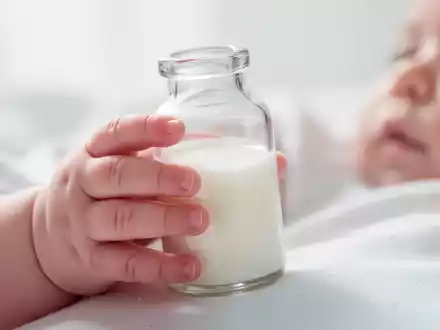 Nahaufnahme der Hand eines Säuglings, die eine Babyflasche mit Milch hält, in einer sanften und hellen Umgebung. - Foto: über boerse-global.de