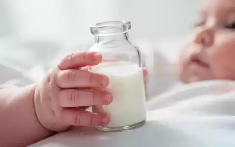 Nahaufnahme der Hand eines Säuglings, die eine Babyflasche mit Milch hält, in einer sanften und hellen Umgebung. - Foto: über boerse-global.de