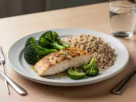 Ein ausgewogener, gesunder Ernährungsplan mit magerem Fisch, grünem Gemüse, Vollkornprodukten und einem Glas Wasser auf einem Holztisch. - Foto: über boerse-global.de