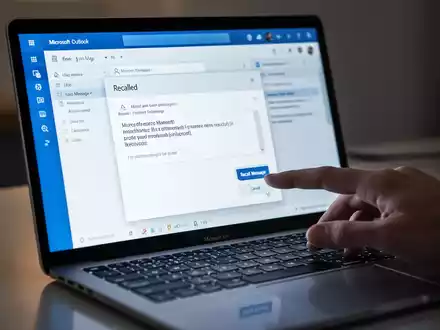 A close-up of a laptop screen showing the Microsoft Outlook interface with an email recall message and a hand hovering over the 'Recall Message' button. - Foto: über boerse-global.de
