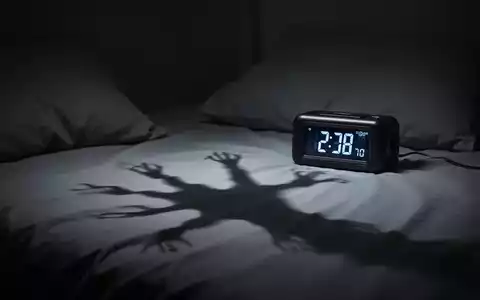 Ein dunkles Schlafzimmer mit einer digitalen Uhr, die frühe Morgenstunden anzeigt, und einem Schatten auf dem Bett. - Foto: über boerse-global.de