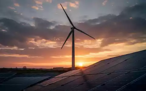 Eine einzelne Windkraftanlage vor einem dramatischen Sonnenuntergang mit Solarmodulen im Vordergrund. - Foto: über boerse-global.de
