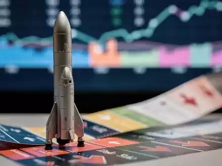 Eine Miniaturrakete von SpaceX steht auf einem Börsentickerband, im Hintergrund verschwommene Finanzdaten und Charts. - Foto: über boerse-global.de