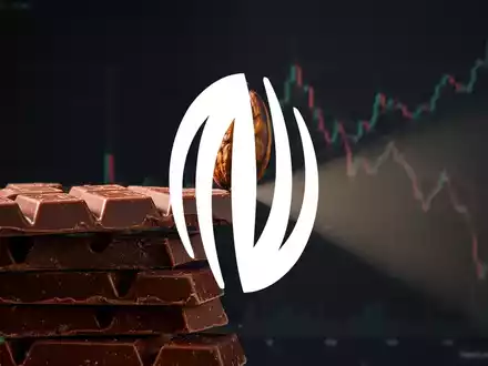 Eine einzelne Kakaobohne balanciert auf einem Stapel Schokoriegel, mit einem absteigenden Börsenchart im Hintergrund. - Foto: über boerse-global.de