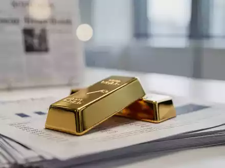 Ein glänzender Goldbarren auf einem Stapel Finanzdokumente mit verschwommenen Inflationsdaten im Hintergrund. - Foto: über boerse-global.de