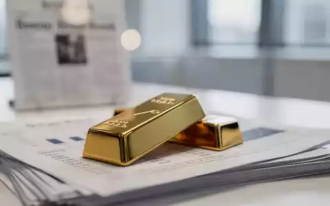 Ein glänzender Goldbarren auf einem Stapel Finanzdokumente mit verschwommenen Inflationsdaten im Hintergrund. - Foto: über boerse-global.de