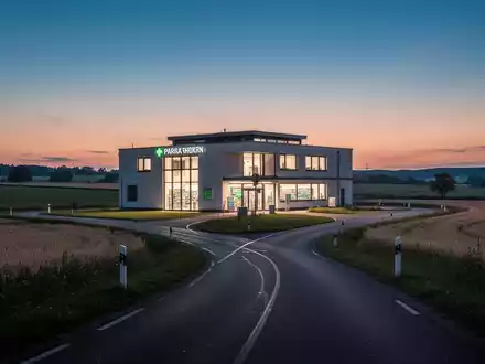 Ein modernes Apothekengebäude bei Dämmerung in einer ländlichen deutschen Landschaft mit einer langen Straße, die dorthin führt. - Foto: über boerse-global.de