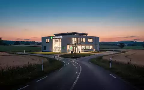 Ein modernes Apothekengebäude bei Dämmerung in einer ländlichen deutschen Landschaft mit einer langen Straße, die dorthin führt. - Foto: über boerse-global.de