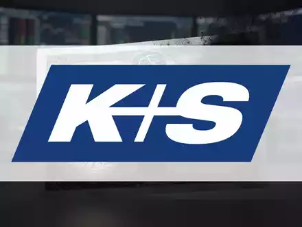 Eine K+S-Aktienanleihe, teilweise im Schatten, vor einem verschwommenen, gedämpften Finanzbürohintergrund. - Foto: über boerse-global.de