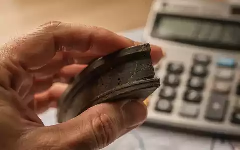 Nahaufnahme einer Hand, die eine Gummidichtung hält, mit einem Taschenrechner und Zahlen im unscharfen Hintergrund. - Foto: über boerse-global.de
