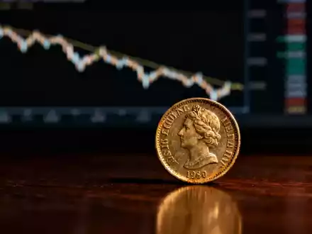 Eine einzelne, leicht abgenutzte schottische Pfundmünze auf einer dunklen Holzoberfläche, im Hintergrund eine verschwommene Finanzgrafik. - Foto: über boerse-global.de