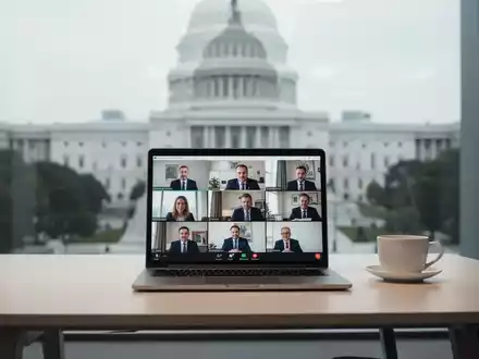 Ein moderner Schreibtisch mit Laptop, der eine Videokonferenz zeigt, und einer Kaffeetasse, im Hintergrund ein Regierungsgebäude. - Foto: über boerse-global.de