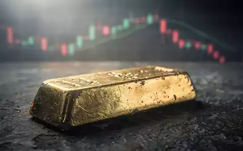 Ein einzelner, leicht angelaufener Goldbarren auf dunklem Untergrund, mit unscharfen Börsencharts im Hintergrund, die einen Abwärtstrend andeuten. - Foto: über boerse-global.de