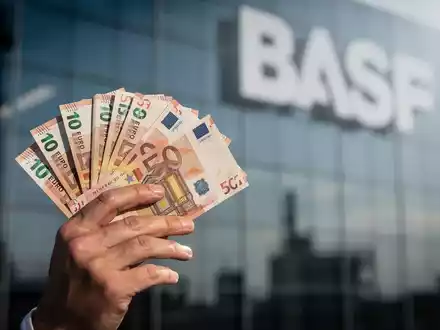 Eine Hand hält einen Stapel Euro-Banknoten, im unscharfen Hintergrund ist das BASF-Logo zu erkennen. - Foto: über boerse-global.de