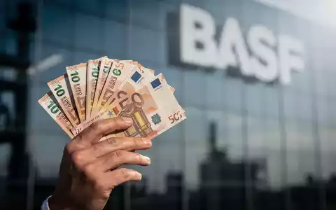 Eine Hand hält einen Stapel Euro-Banknoten, im unscharfen Hintergrund ist das BASF-Logo zu erkennen. - Foto: über boerse-global.de
