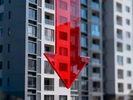 Ein modernes Wohngebäude mit einem großen, roten, nach unten zeigenden Pfeil davor, der einen Rückgang symbolisiert. - Foto: über boerse-global.de