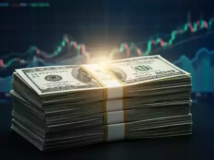 Ein großer Stapel US-Dollar-Banknoten mit unscharfen Finanzdiagrammen im Hintergrund, der einen Aktienrückkauf symbolisiert. - Foto: über boerse-global.de