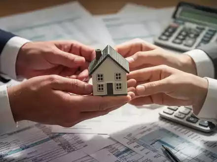 Nahaufnahme der Hände eines Ehepaares, die eine kleine Hausfigur über Finanzdokumenten austauschen, symbolisiert steuerfreie Immobilienübertragung. - Foto: über boerse-global.de