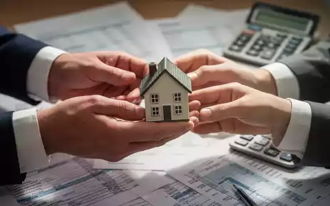 Nahaufnahme der Hände eines Ehepaares, die eine kleine Hausfigur über Finanzdokumenten austauschen, symbolisiert steuerfreie Immobilienübertragung. - Foto: über boerse-global.de