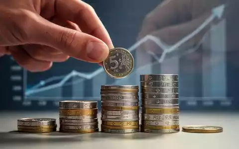 Eine Hand legt eine Münze auf einen Stapel Schweizer Franken, mit einem unscharfen Finanzdiagramm im Hintergrund. - Foto: über boerse-global.de