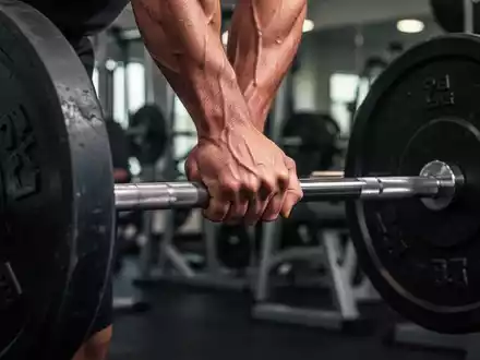 Nahaufnahme einer Hand, die eine schwere Langhantel im Fitnessstudio greift, mit Fokus auf Muskelspannung und Anstrengung. - Foto: über boerse-global.de