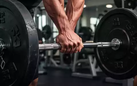 Nahaufnahme einer Hand, die eine schwere Langhantel im Fitnessstudio greift, mit Fokus auf Muskelspannung und Anstrengung. - Foto: über boerse-global.de