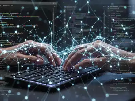 A developer's hands typing on a keyboard, with a glowing neural network overlay and subtle Visual Studio Code interface elements in the background. - Foto: über boerse-global.de