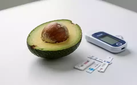Eine halbierte Avocado mit Kern auf weißer Oberfläche, daneben ein Blutzuckermessgerät und Teststreifen. - Foto: über boerse-global.de