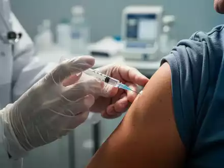 Eine Nahaufnahme zeigt die Hände eines Arztes, der einem Patienten eine Impfung verabreicht, mit Fokus auf Nadel und Arm. - Foto: über boerse-global.de