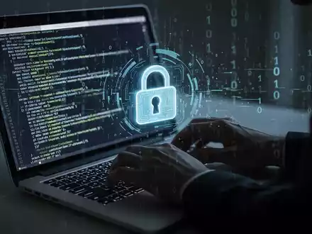 A shadowy figure types on a laptop, code on screen, with a digital lock icon and binary data representing a cybersecurity breach. - Foto: über boerse-global.de