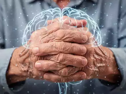 Nahaufnahme der Hände einer älteren Person, die die Gelenke reibt, mit einer dezenten grafischen Überlagerung eines Gehirns. Symbolisiert psychische Belastung bei Arthrose. - Foto: über boerse-global.de
