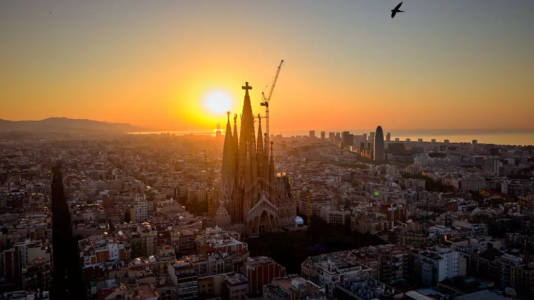 Im Gegenlicht der aufgehenden Sonne ist das Kreuz aus Deutschland auf der Spitze des höchsten Turms der Basilika Sagrada Família in Barcelona gut zu erkennen. (Archivbild) - Bild: Emilio Morenatti/AP/dpa