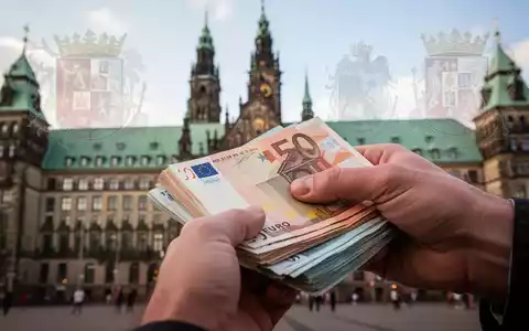 Eine Hand hält einen Stapel Euro-Banknoten, im unscharfen Hintergrund ist das Hamburger Rathaus zu sehen. - Foto: über boerse-global.de