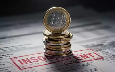 Ein unsicher gestapelter Haufen deutscher Euro-Münzen, im Hintergrund verschwommene Finanzdokumente mit einem roten 'insolvent'-Stempel. - Foto: über boerse-global.de