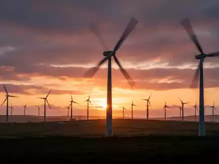 Windpark-Silhouetten vor einem dramatischen Sonnenuntergang auf der Isle of Man, symbolisch für erneuerbare Energien und Preissenkungen. - Foto: über boerse-global.de