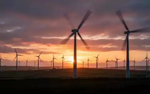Windpark-Silhouetten vor einem dramatischen Sonnenuntergang auf der Isle of Man, symbolisch für erneuerbare Energien und Preissenkungen. - Foto: über boerse-global.de