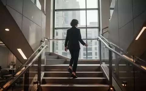 Eine Person steigt achtsam eine moderne Treppe hinauf, mit sanftem Licht, das durch ein Fenster fĂ€llt. Fokus auf ruhige Bewegung. - Foto: ĂŒber boerse-global.de