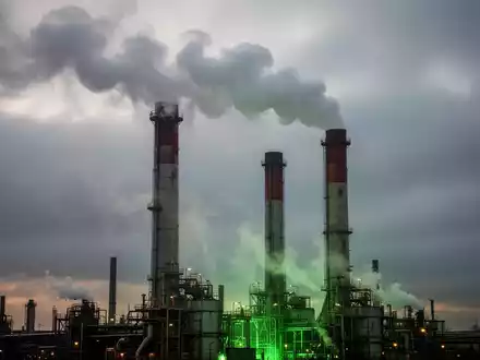 Industrieschornsteine emittieren Dampf und leichten Rauch vor einem dramatischen, bewölkten Himmel mit einem grünen Lichtschein. - Foto: über boerse-global.de