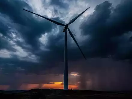 Eine einzelne Windkraftanlage steht still vor einem stürmischen, dramatischen Himmel bei Sonnenuntergang. - Foto: über boerse-global.de