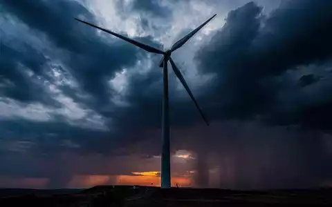 Eine einzelne Windkraftanlage steht still vor einem stürmischen, dramatischen Himmel bei Sonnenuntergang. - Foto: über boerse-global.de