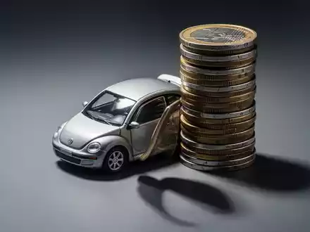 Ein Miniatur-Volkswagen-Modell ist teilweise von einem Stapel riesiger Euro-Münzen verdeckt, die hohe Kosten symbolisieren. - Foto: über boerse-global.de