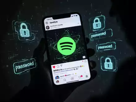 Eine Hand hält ein Smartphone mit einem verzerrten Spotify-Logo auf einem Social-Media-Feed, umgeben von digitalen Schloss- und Passwort-Symbolen. - Foto: über boerse-global.de