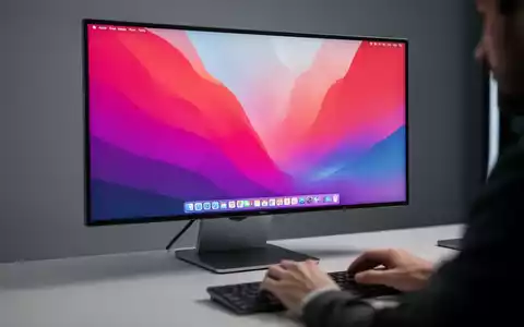 A close-up of a modern ultrawide computer monitor displaying the macOS desktop, with hands typing on a keyboard. - Foto: über boerse-global.de