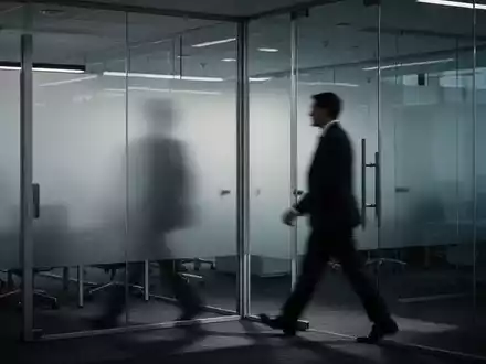Ein gedämpft beleuchtetes, modernes Büro mit einer verschwommenen Figur, die an undurchsichtigen Glaswänden vorbeigeht. - Foto: über boerse-global.de