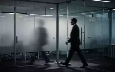 Ein gedämpft beleuchtetes, modernes Büro mit einer verschwommenen Figur, die an undurchsichtigen Glaswänden vorbeigeht. - Foto: über boerse-global.de