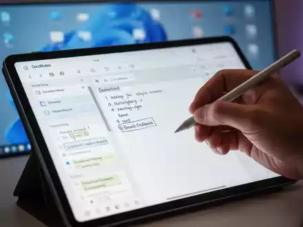A hand holding a stylus, writing on a tablet displaying the GoodNotes app, with a blurred Windows 11 desktop in the background. - Foto: über boerse-global.de