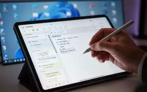 A hand holding a stylus, writing on a tablet displaying the GoodNotes app, with a blurred Windows 11 desktop in the background. - Foto: über boerse-global.de